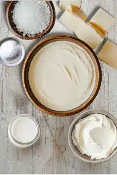 Ingredients for Cheesecake Fondue, including cream cheese, sweetened condensed milk, heavy cream, vanilla extract, powdered sugar, and a pinch of salt, displayed on a rustic wooden surface.