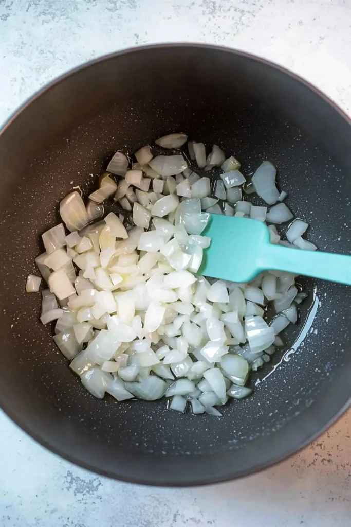 Chopped onions being sautéed in a pot with a turquoise spatula stirring.