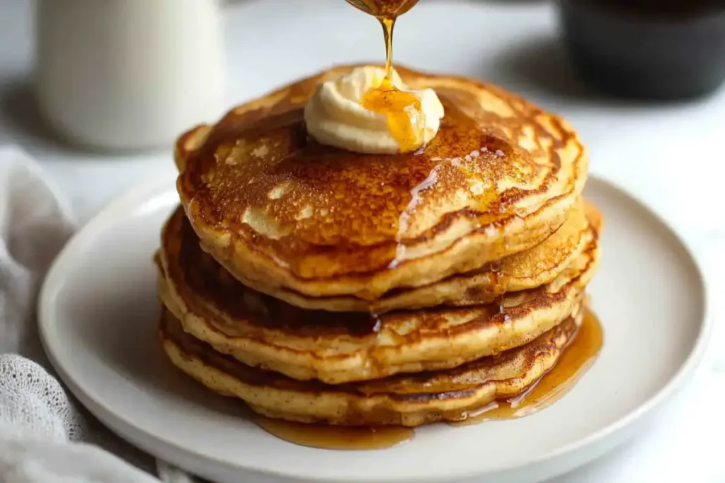 Cinnamon swirl pancakes topped with a pat of butter and a drizzle of maple syrup, served alongside a cup of coffee.