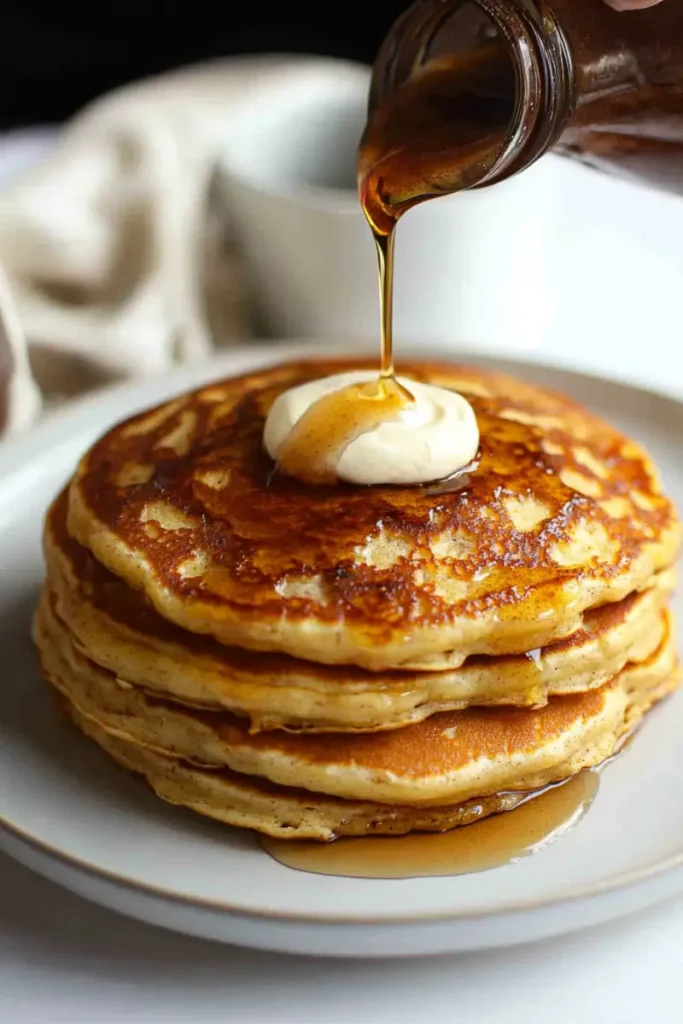 A stack of fluffy cinnamon swirl pancakes topped with butter and a drizzle of syrup.