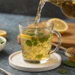 Lemon balm tea with fresh lemon slices, mint leaves, and honey being poured into a glass cup.